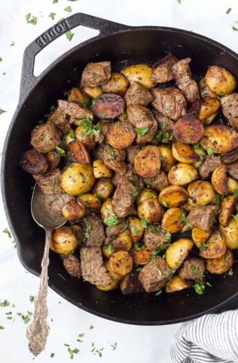 Garlic butter steak bites and baby potatoes inside of a skillet with a metal spoon