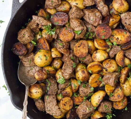 Garlic butter steak bites and baby potatoes inside of a skillet with a metal spoon