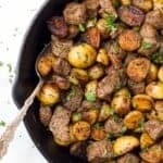 A spoon in a skillet with garlic butter steak bites and potatoes