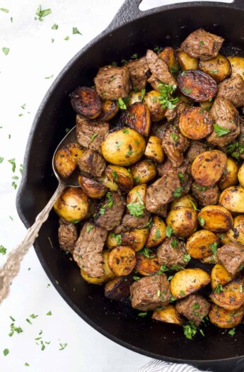 A spoon in a skillet with garlic butter steak bites and potatoes