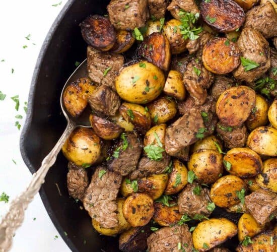 A spoon in a skillet with garlic butter steak bites and potatoes