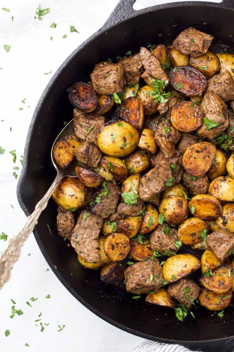 A spoon in a skillet with garlic butter steak bites and potatoes