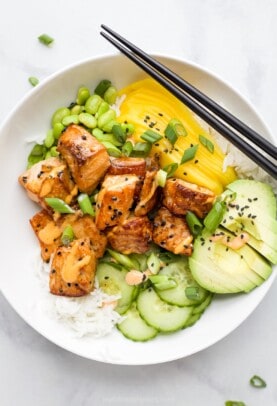 A close-up shot of a rice bowl with fish, mango, avocado, cucumber and more