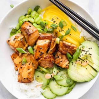 A close-up shot of a rice bowl with fish, mango, avocado, cucumber and more