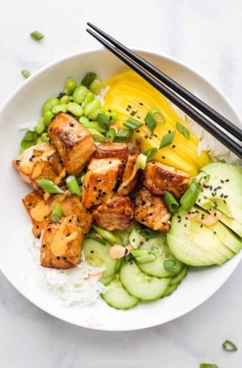 A close-up shot of a rice bowl with fish, mango, avocado, cucumber and more