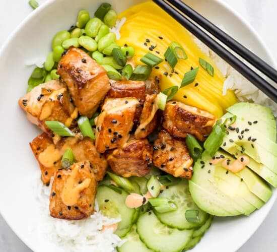 A close-up shot of a rice bowl with fish, mango, avocado, cucumber and more