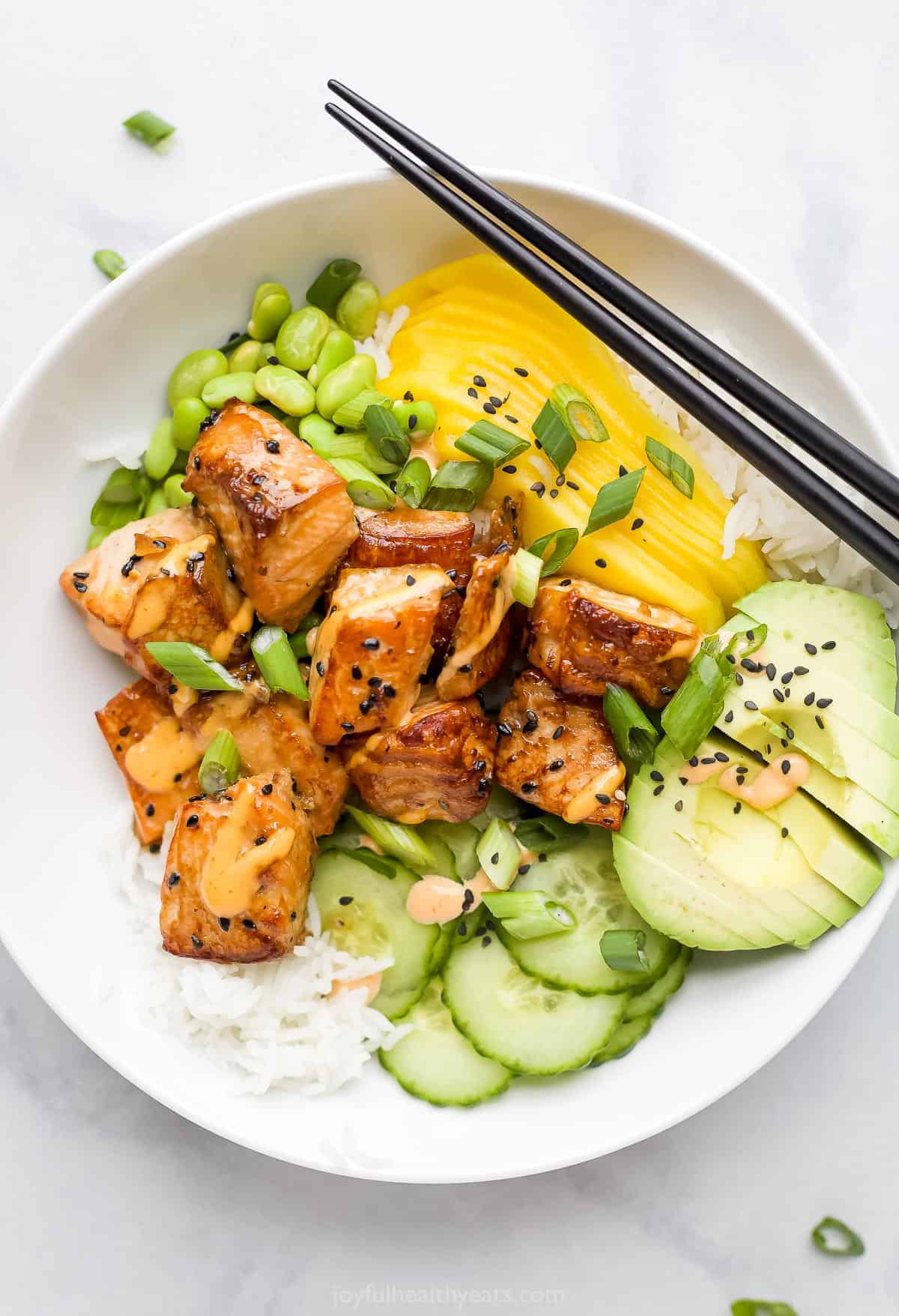 A close-up s،t of a rice bowl with fish, mango, avocado, cu،ber and more