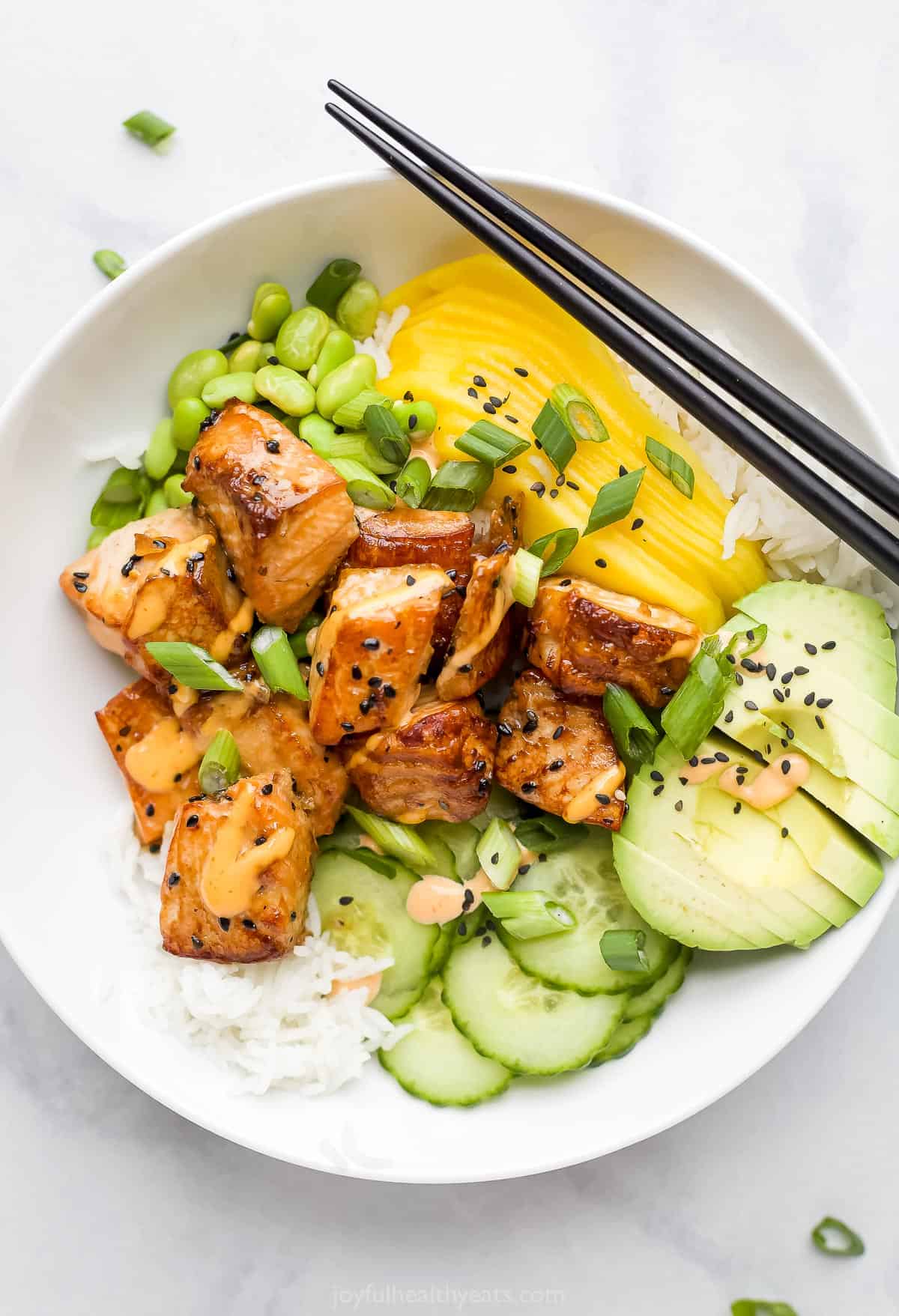 A close-up shot of a rice bowl with fish, mango, avocado, cucumber and more