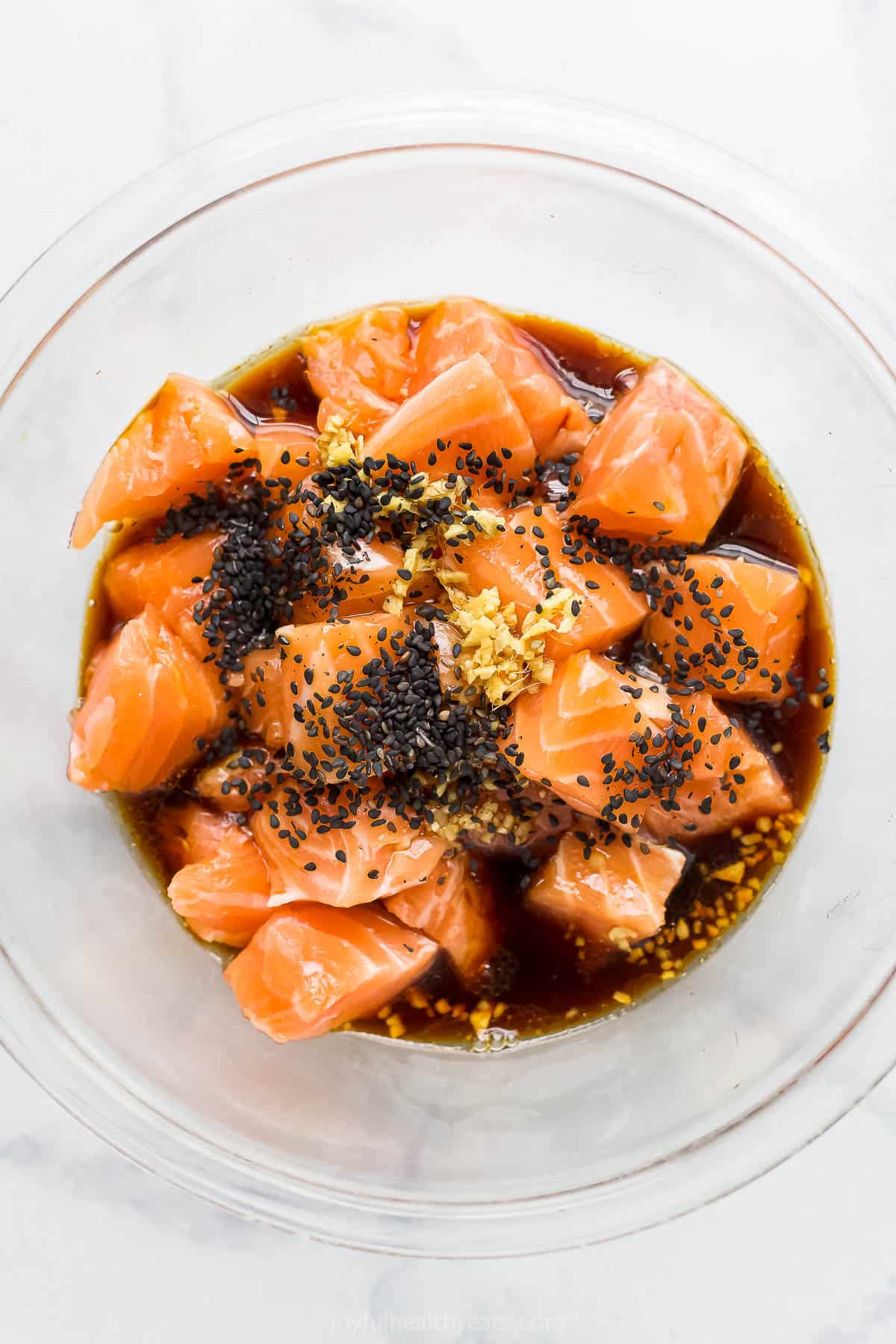 Cubes of uncooked salmon inside of a glass bowl with the Japanese-inspired marinade