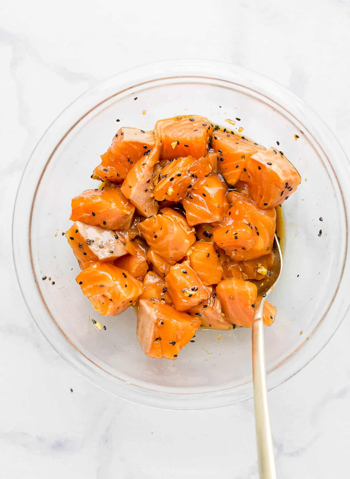 Unbaked salmon being mixed with the seasoning blend by a metal spoon