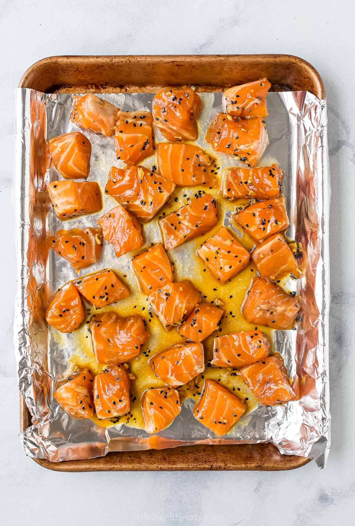Marinated cubes of salmon on top of a metal cookie sheet lined with aluminum foil