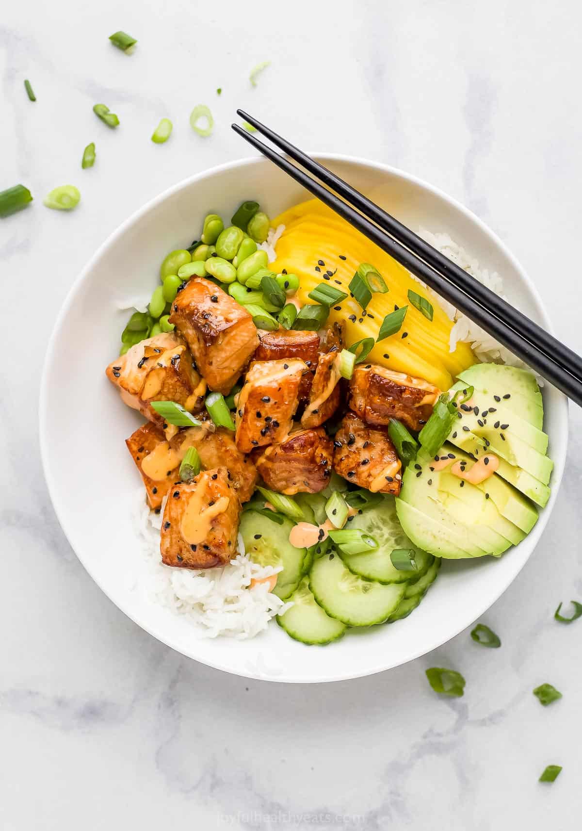 A poke bowl on a black and white countertop with a pair of black chopsticks on top of it