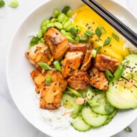 A salmon poke bowl garnished with black sesame seeds on top of a marble counter