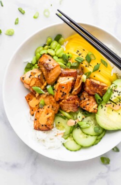 A salmon poke bowl garnished with black sesame seeds on top of a marble counter