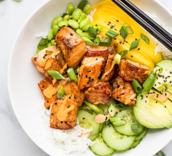 A salmon poke bowl garnished with black sesame seeds on top of a marble counter