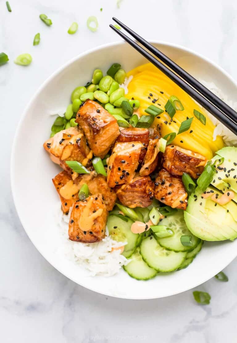 A salmon poke bowl garnished with black sesame seeds on top of a marble counter