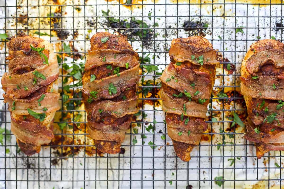 Cooked chicken breasts wrapped in bacon on a baking sheet