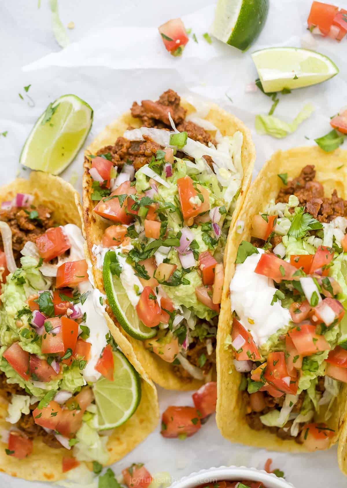 a collection of ground beef tacos topped with lettuce, avocado, pico and sour cream