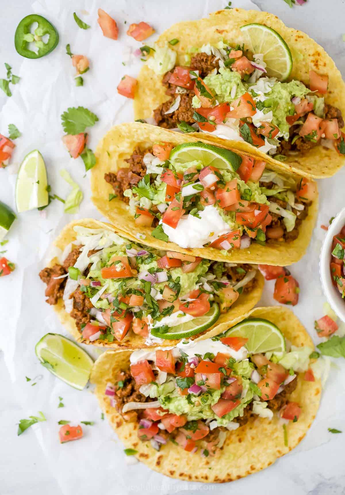 four ground beef tacos with toppings on them