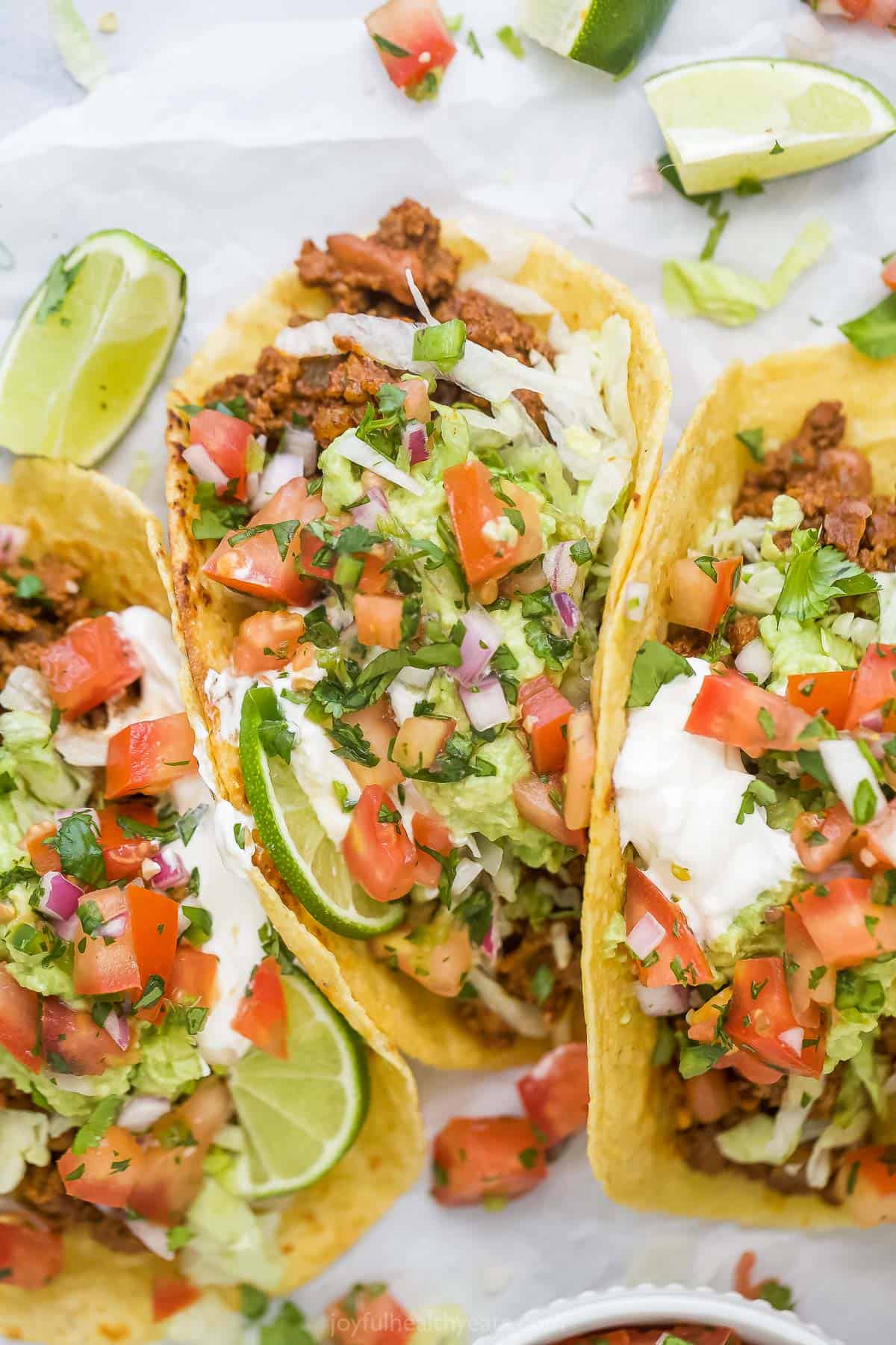 closeup of ground beef tacos topped with lettuce, pico de gallo, avocado and sour cream