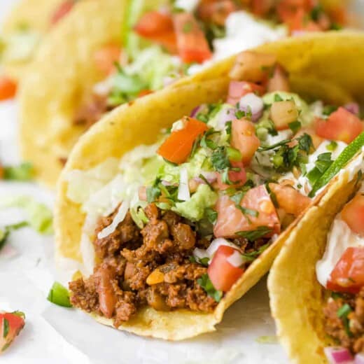 a group of ground beef tacos topped with avocado, sour cream, pico de gallo