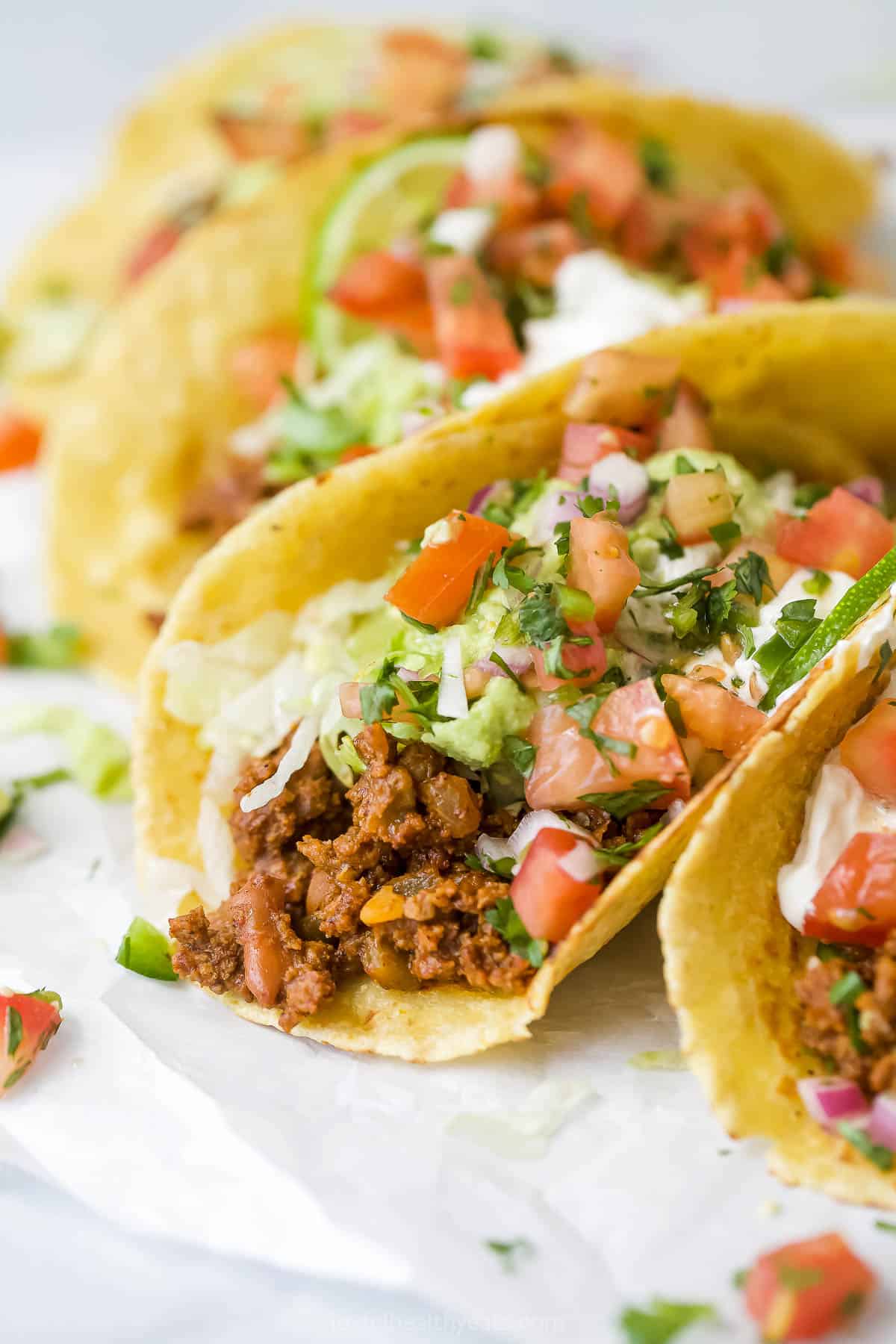 a group of ground beef tacos topped with avocado, sour cream, pico de gallo