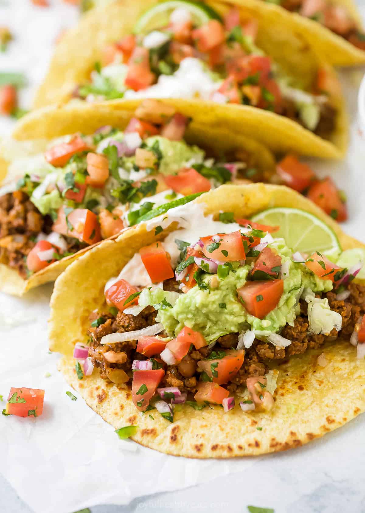 close up photo of ground beef tacos topped with avocado, pico de gallo and sour cream