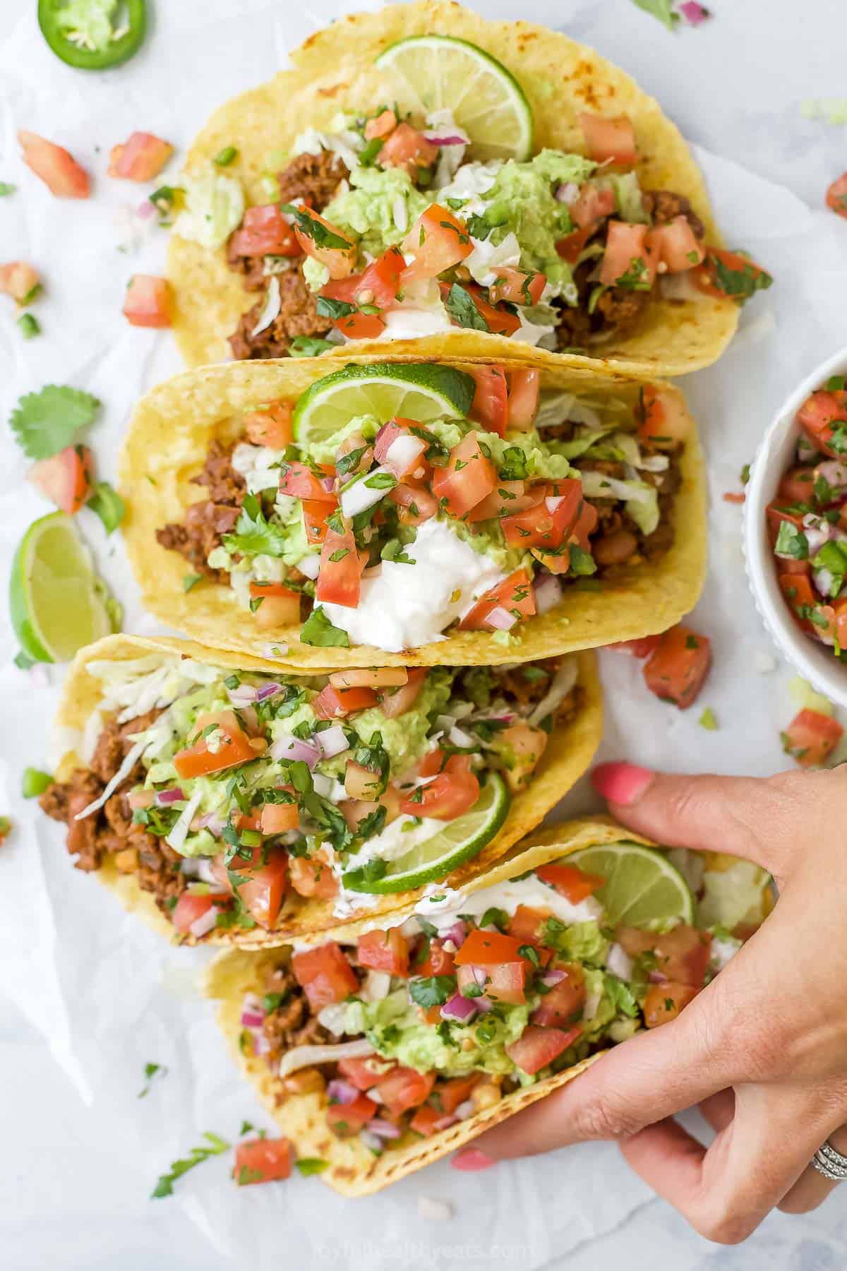 hand grabbing ground beef tacos with toppings