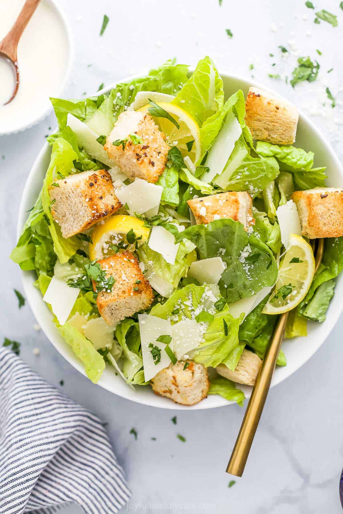 A bowl of caesar salad with a golden spoon inside