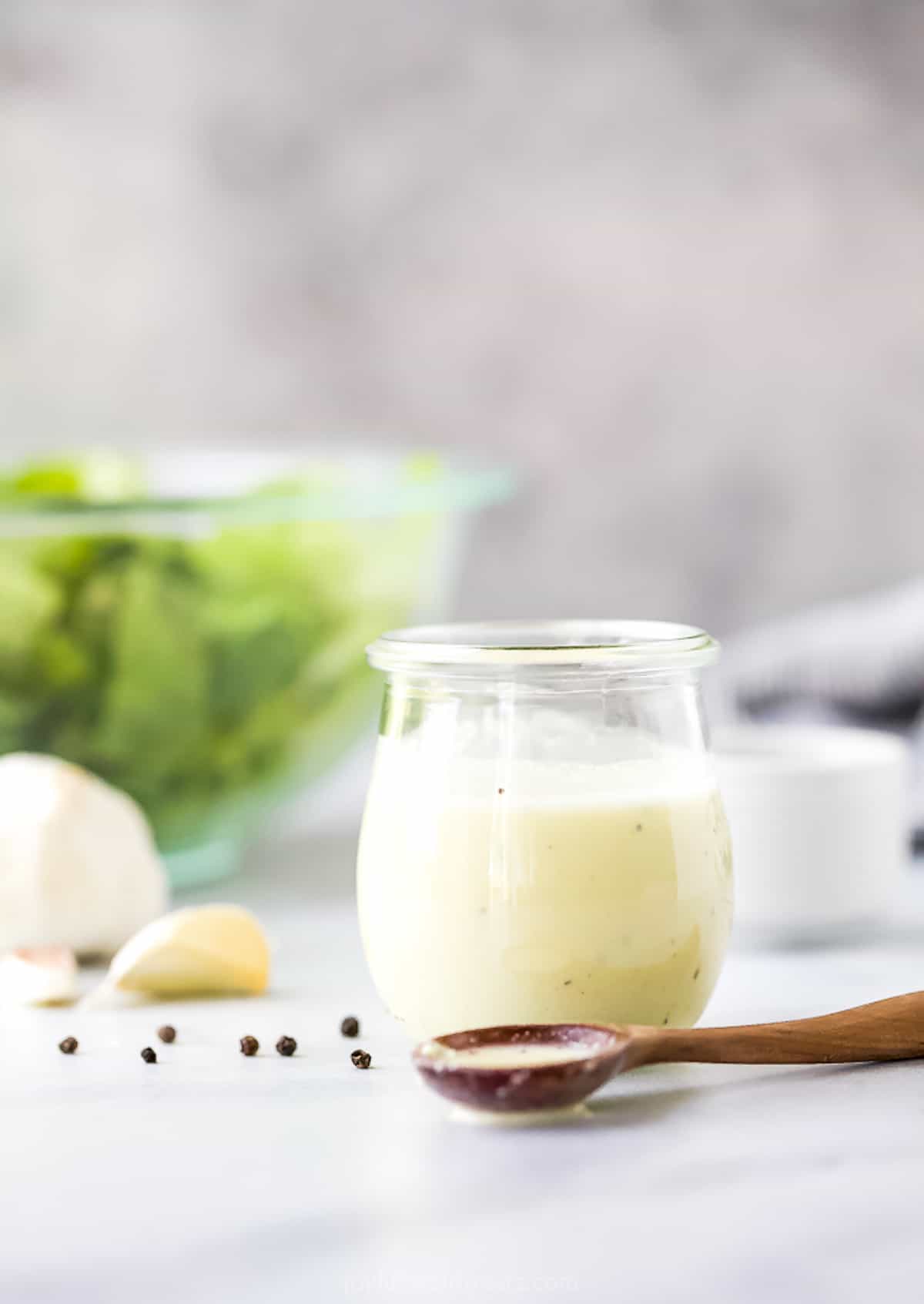 A glass full of homemade caesar dressing with a spoonful of dressing on the counter beside it