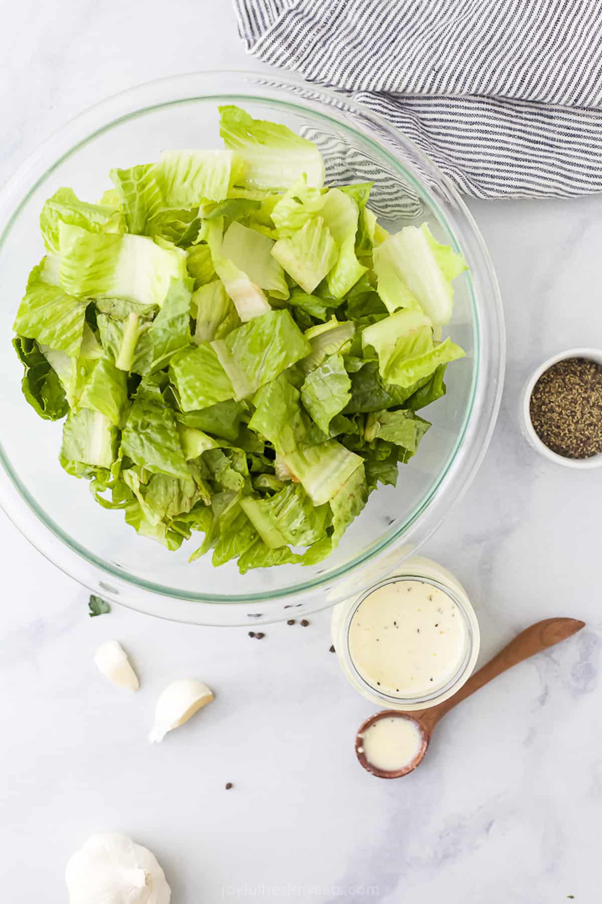 Chopped lettuce in a mixing bowl beside a jar of homemade dressing