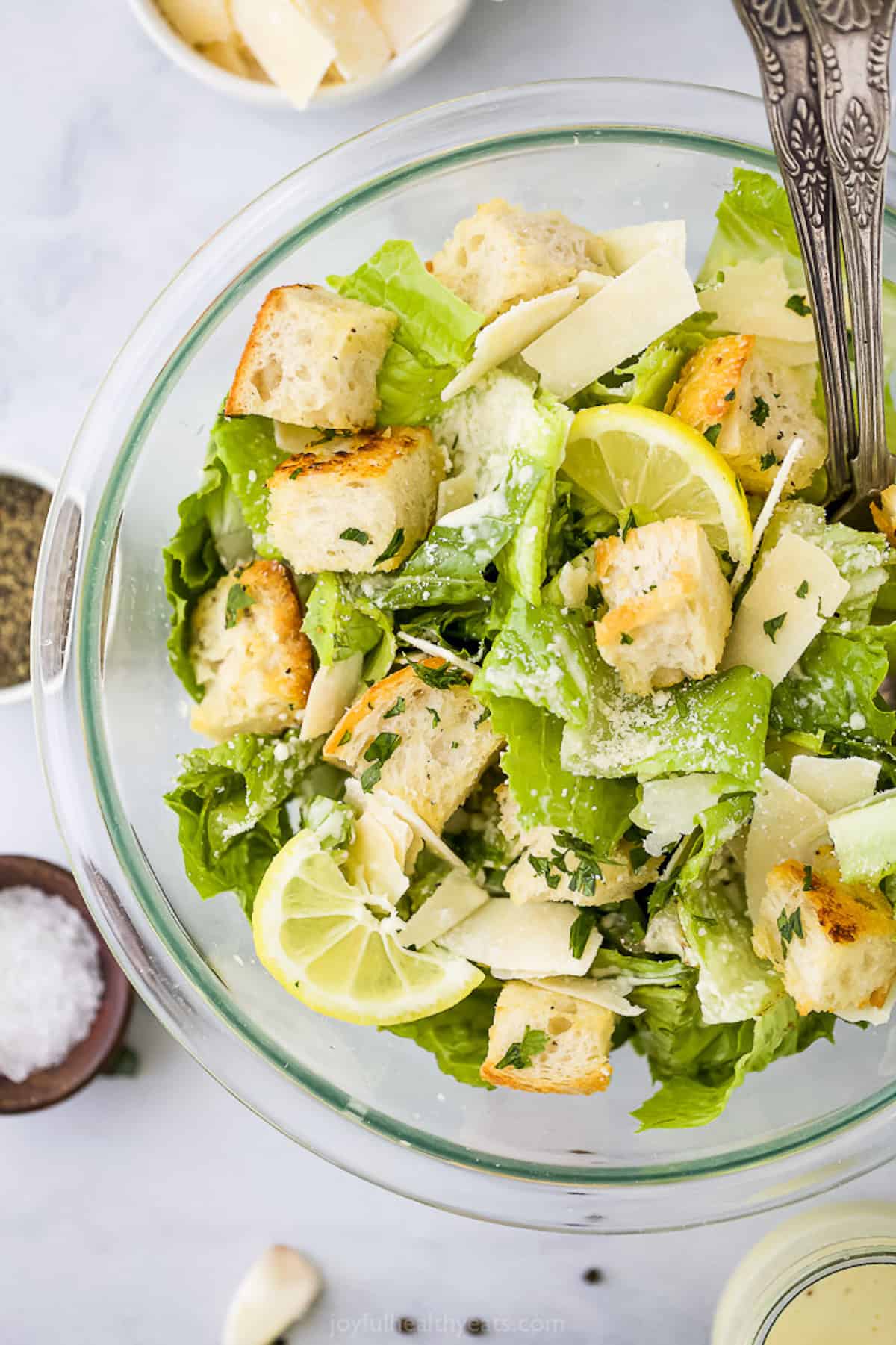 Caesar salad inside of a large glass mixing bowl with two forks inside