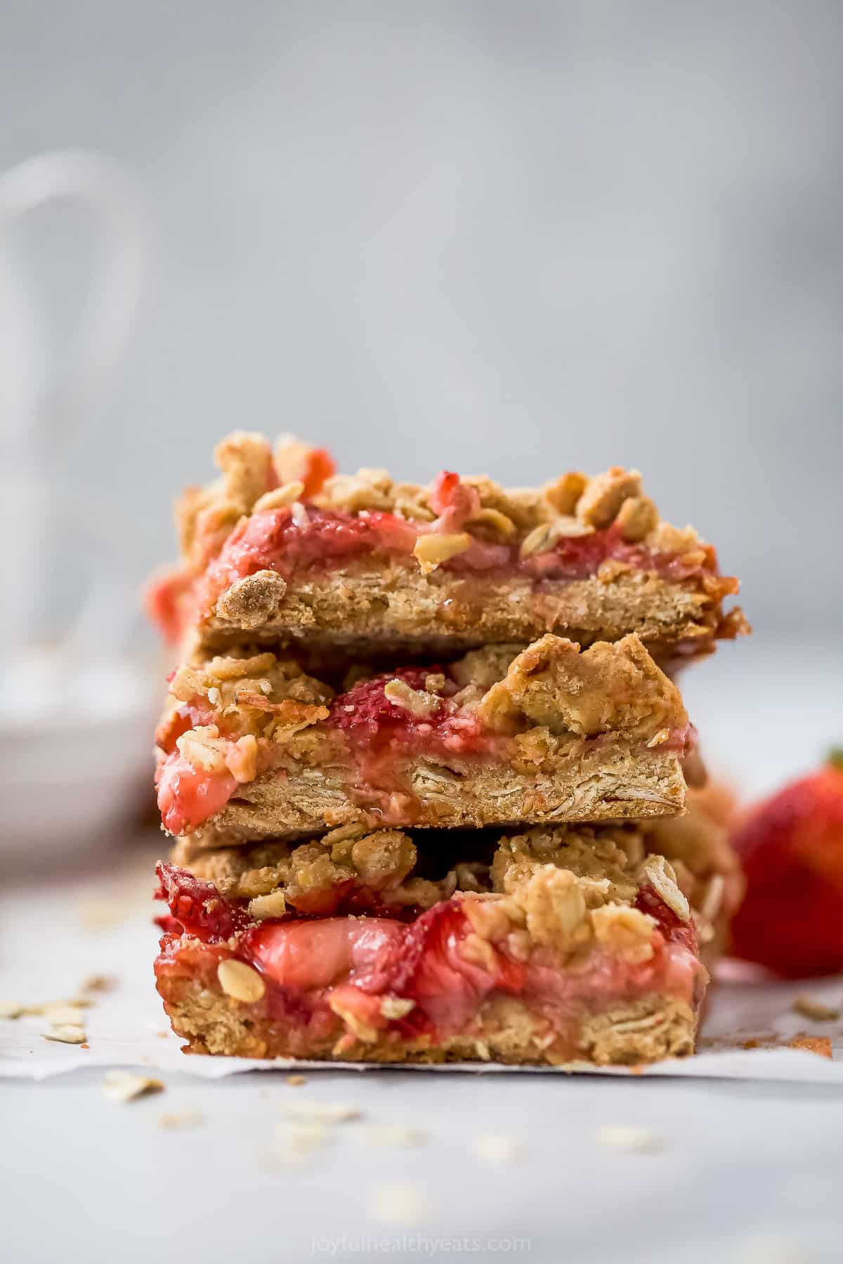 Three strawberry oatmeal bars stacked on top of one another with a fresh berry beside the stack