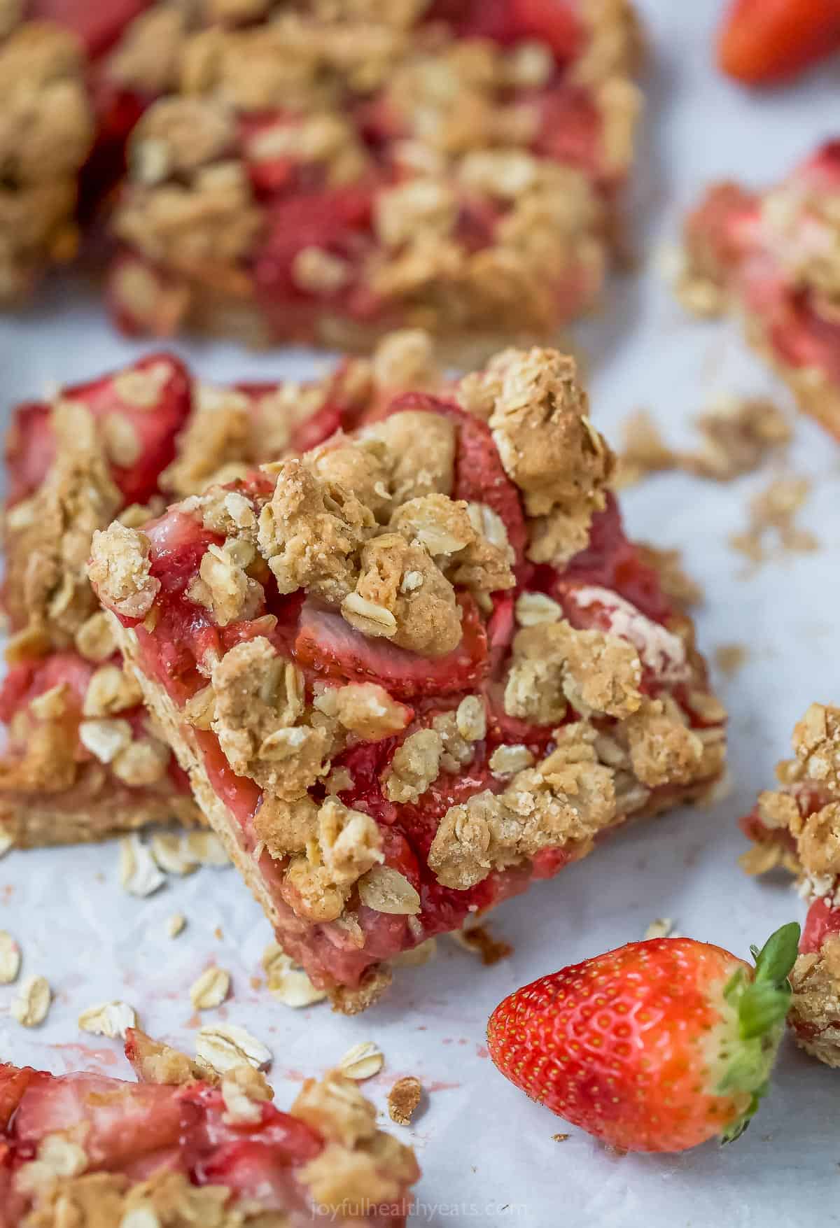 A strawberry oatmeal bar leaning against another bar with a fresh strawberry in the foreground