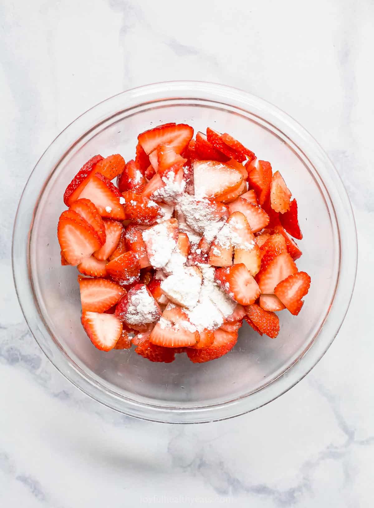 A bowl of sliced strawberries with white whole wheat flour poured on top