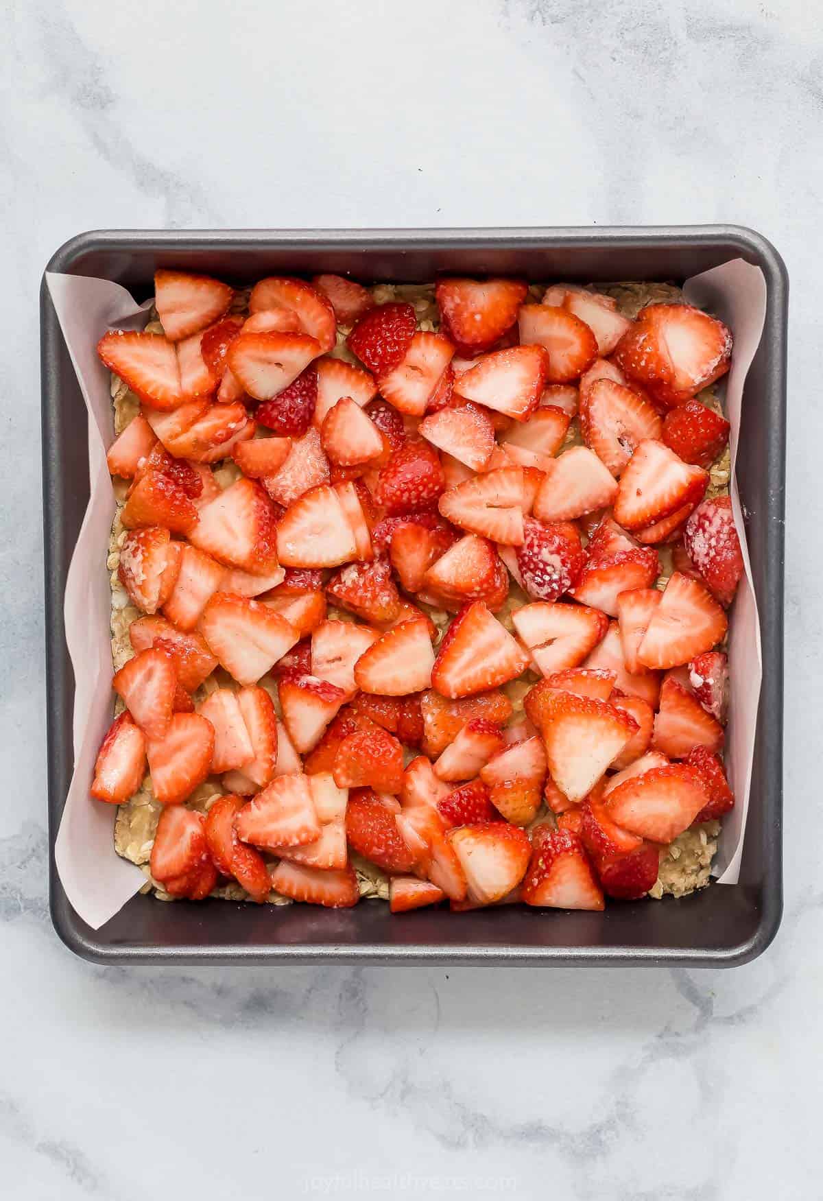 The strawberry filling spread on top of the crust mixture in the lined and greased baking dish