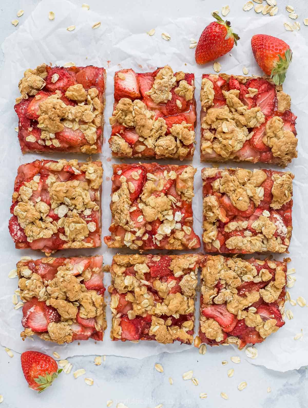Nine strawberry oatmeal bars on top of a sheet of parchment paper