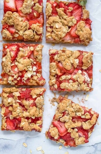 Six strawberry oat bars on a marble countertop with a sheet of parchment paper underneath them