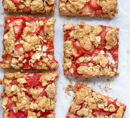 Six strawberry oat bars on a marble countertop with a sheet of parchment paper underneath them