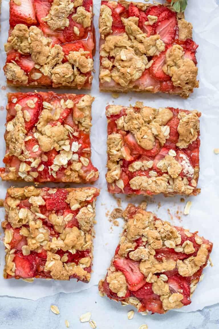 Six strawberry oat bars on a marble countertop with a sheet of parchment paper underneath them