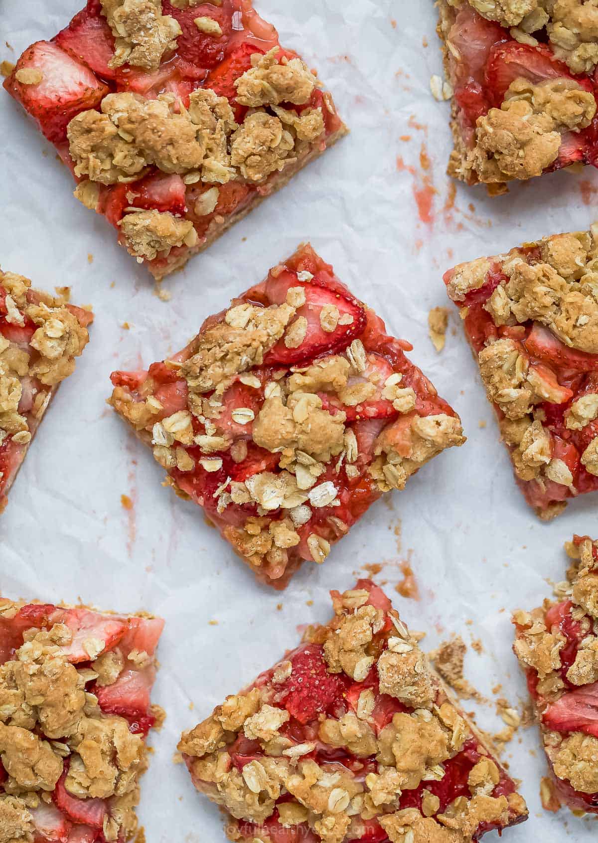 A bunch of homemade strawberry oatmeal bars on top of a sheet of parchment paper