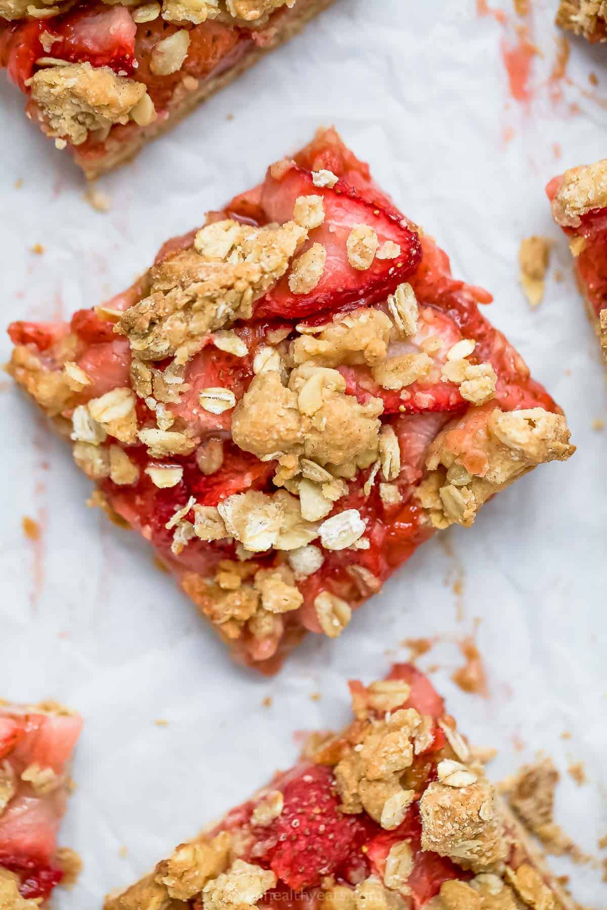 A close-up shot of a strawberry oatmeal bar with portions of other bars shown beside it