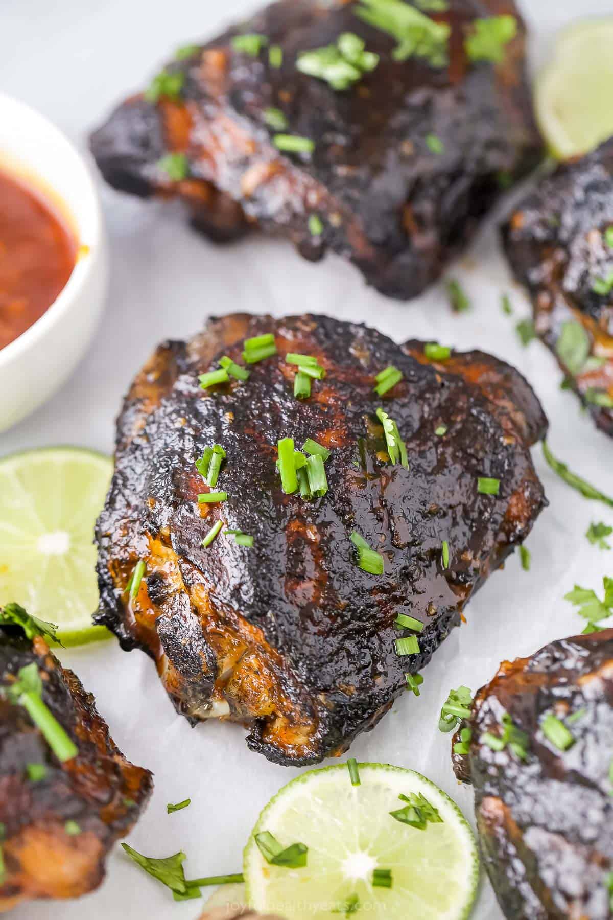 Grilled honey sriracha chicken thighs on a sheet of parchment paper with three fresh lime slices