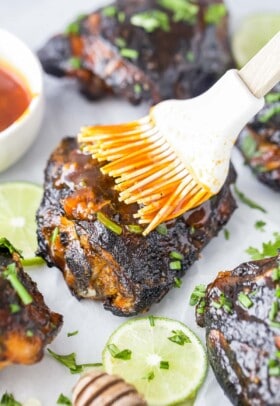 Extra honey sriracha sauce being brushed onto a grilled chicken thigh