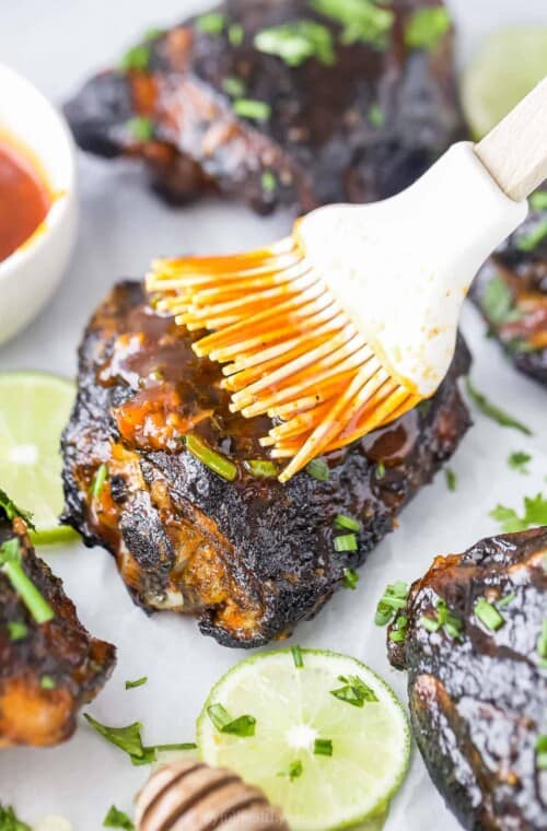 Extra honey sriracha sauce being brushed onto a grilled chicken thigh