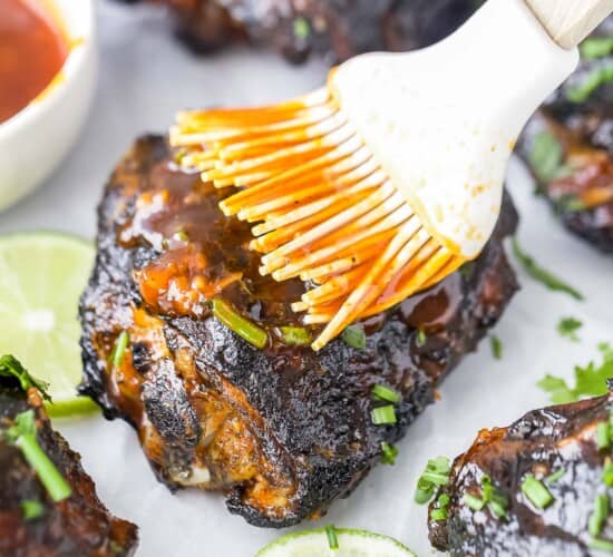 Extra honey sriracha sauce being brushed onto a grilled chicken thigh