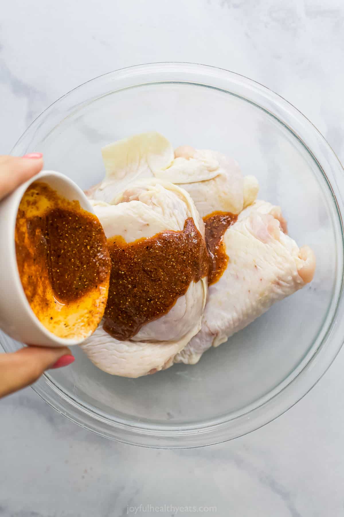 spice rub being poured over chicken thighs