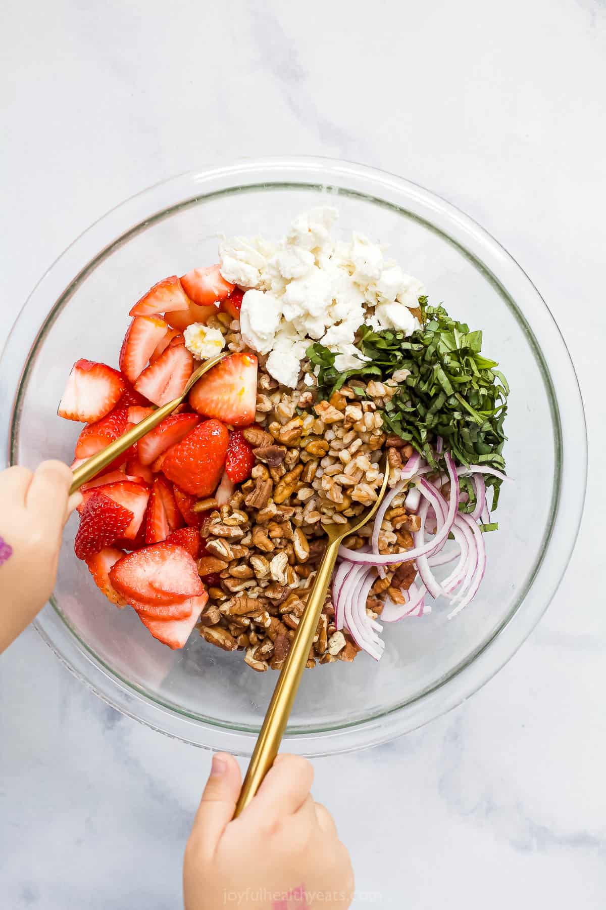 Two spoons with long handles being used to toss the dressing with the salad