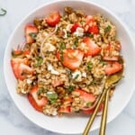 A strawberry farro salad in a serving bowl on top of a marble counter