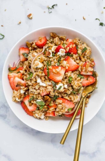 A strawberry farro salad in a serving bowl on top of a marble counter